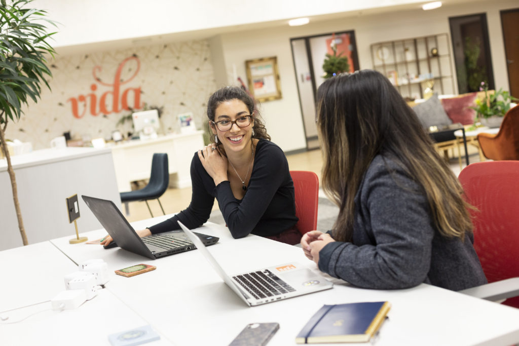 two smiling women working at a desk at vida coworking