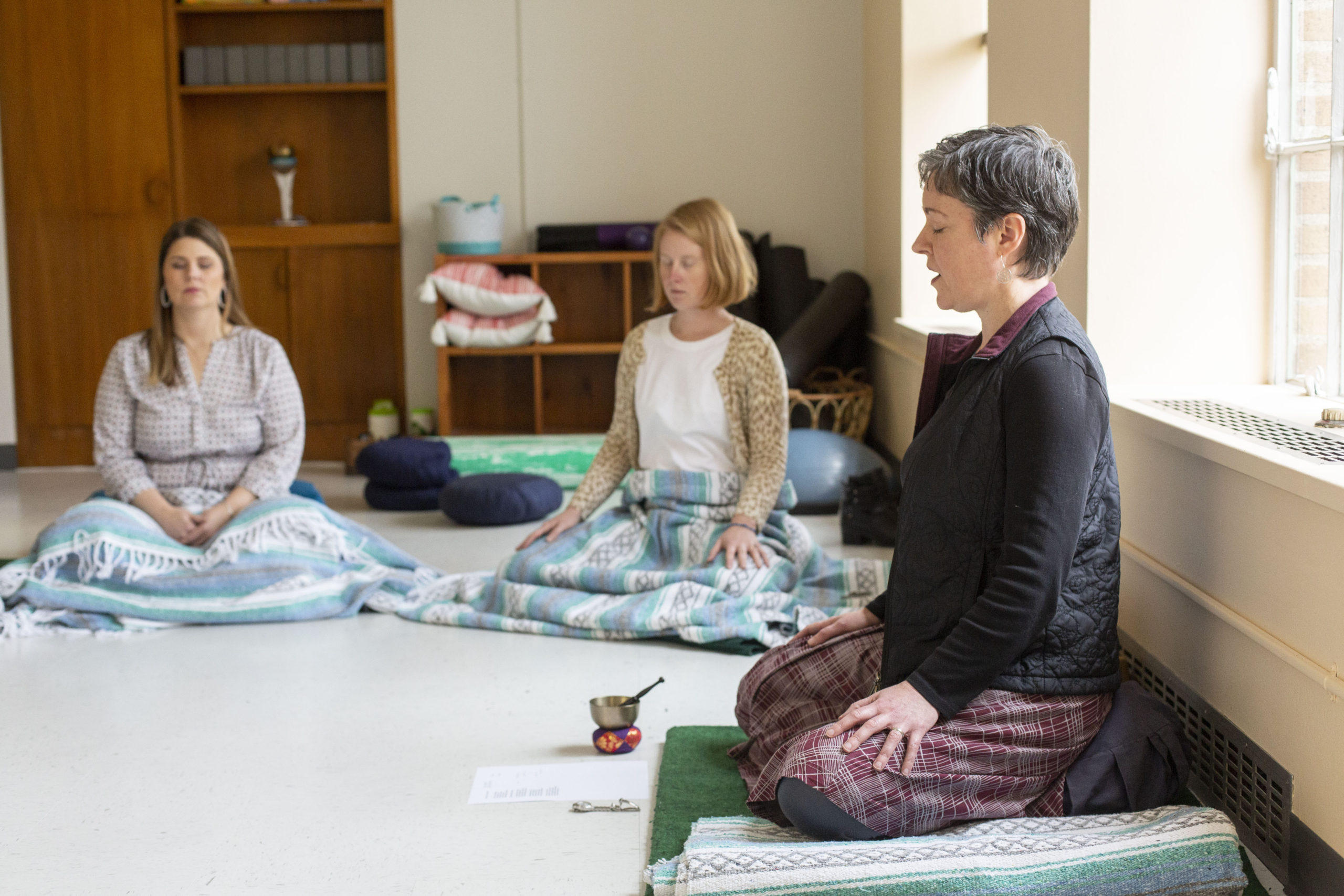 Three people sitting in a cross legged yoga pose with their eyes closed