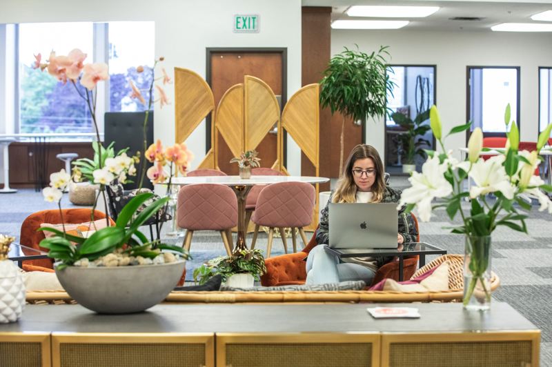 A woman sitting on a couch working on her laptop in the middle of a vibrant coworking office