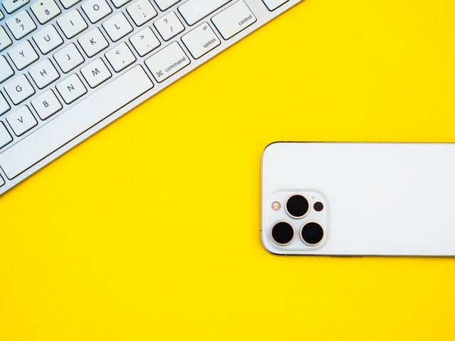 a computer keyboard and iPhone against a yellow background