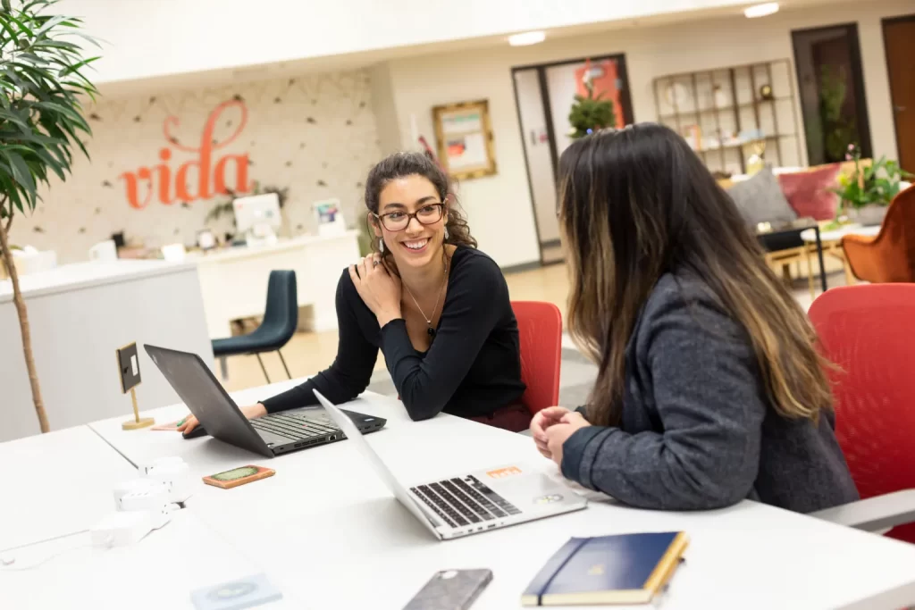 Open coworking space at VIDA Portland featuring stylish shared workstations and natural light. Two women working on their laptops and building connection and community at VIDA Coworkiing Beaverton.