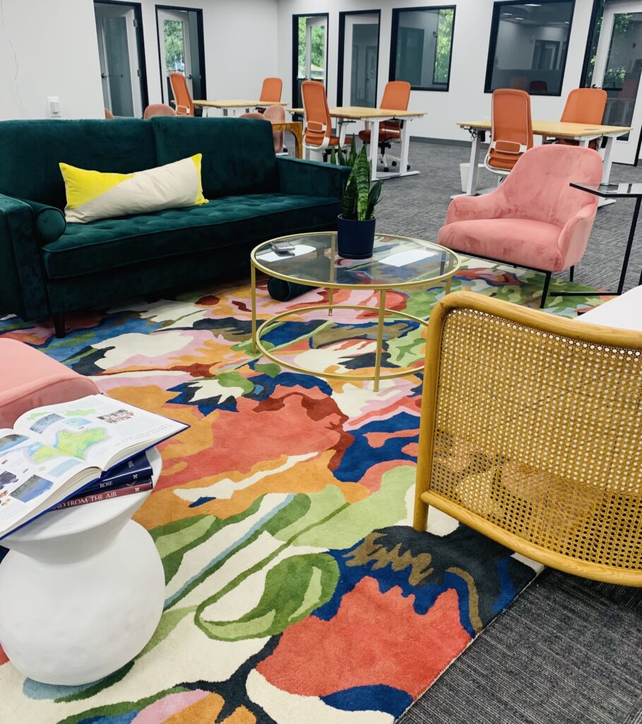 The interior of the Beaverton VIDA office, featuring a green velvet couch, a bright colorful rug, and orange chairs.