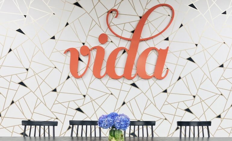 A gold and white patterned wall with the orange VIDA logo on it.