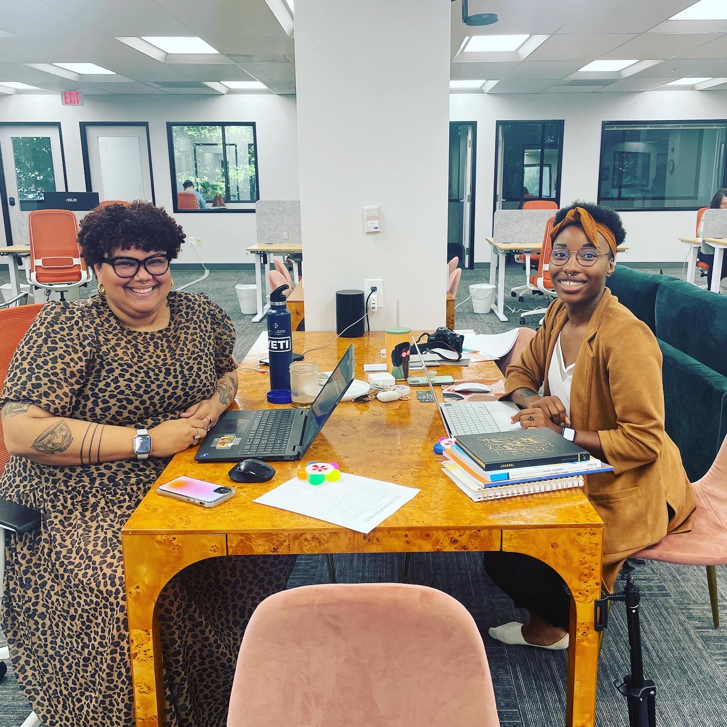 Two VIDA Coworking members collaborating at a shared desk, surrounded by notebooks and work materials.
