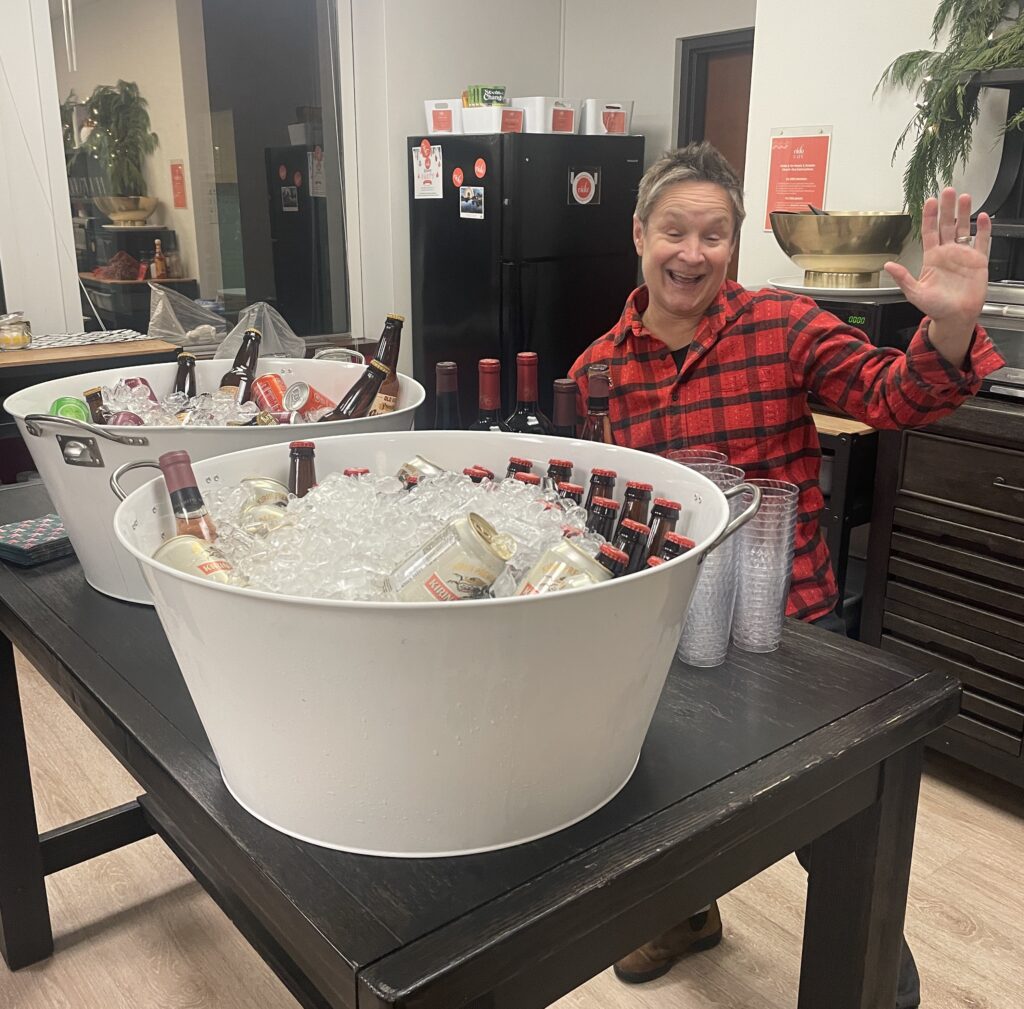 A woman posing behind two giant drink cooler barrels that are filled with ice and wine bottles