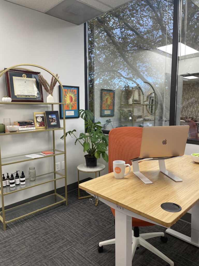 An adjustable sit/stand desk with a bookshelf full of quirky tchotchkes behind it