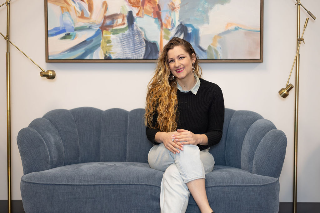 A woman sitting on a couch with bright paintings on the wall behind her