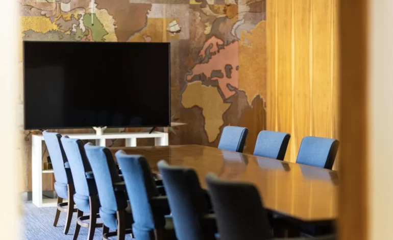 VIDA NE's conference room, featuring a long wood table, sleek velvet chairs, a large tv, and fun wallpaper.