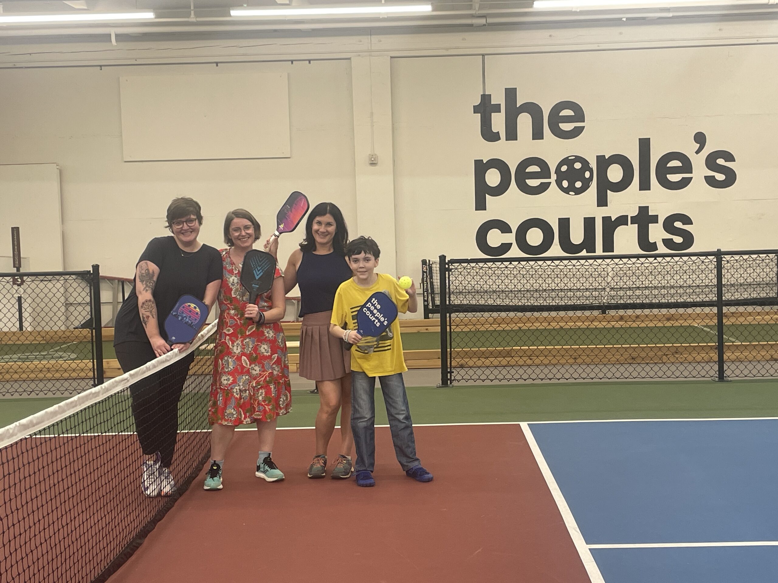 Two adults and two kids holding paddles at The People's Court pickleball courts