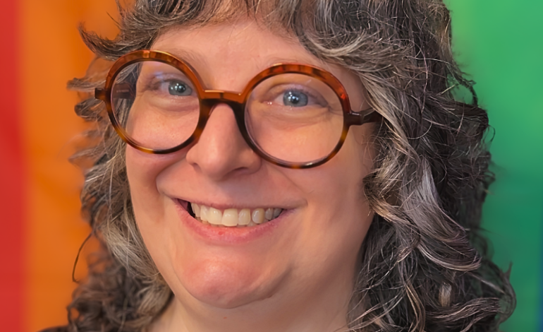 Headshot of Joann, VIDA Virtual Community Manager, smiling in round tortoiseshell glasses against a colorful rainbow-striped backdrop.