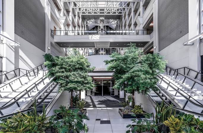 Bright multi-story atrium at Montgomery Park in NW Portland with skylight, open metal walkways, and lush greenery flanking the entrance. Home of VIDA Coworking's third location.